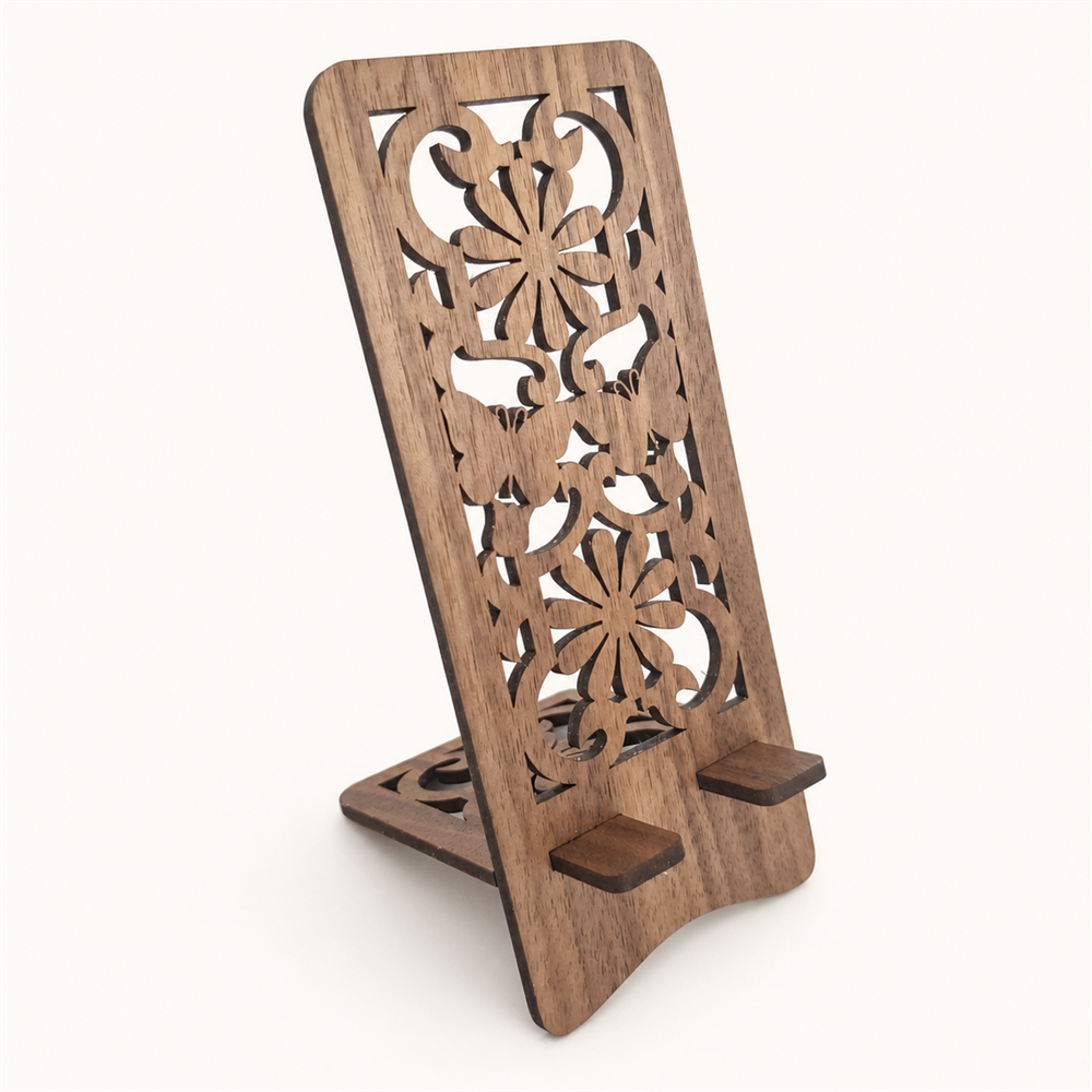 A wooden phone stand with an ornate laser-cut floral pattern on the back panel and two small support feet at the base, shown on a plain light background.