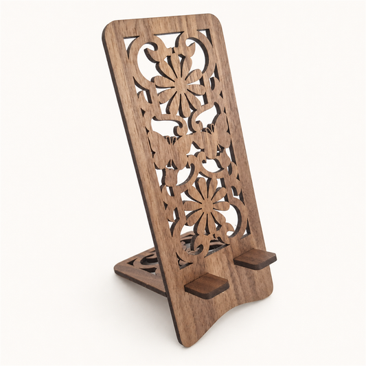 A wooden phone stand with an ornate laser-cut floral pattern on the back panel and two small support feet at the base, shown on a plain light background.