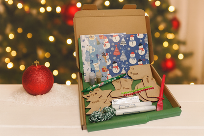 Open cardboard box with Christmas-themed stationery items on a table with festive lights in the background