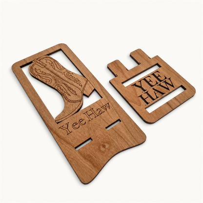 Two wooden stand pieces laying flat on a plain light background. One piece features a cowboy boot with engraving and etched with 'Yee Haw', while the other has the words 'YEE HAW' in a block-style design.