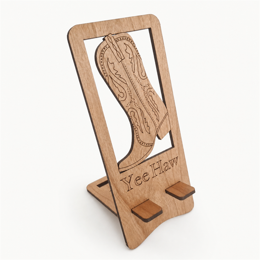 A wooden phone stand with a laser-engraved cowboy boot design and the text 'YeeHaw' on the front, displayed on a clean white background.
