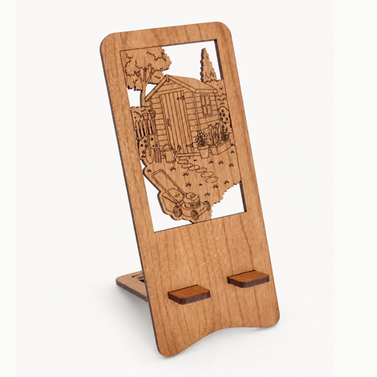 A wooden phone stand with a laser-engraved shed and gardening picture, shown on a plain off-white background.