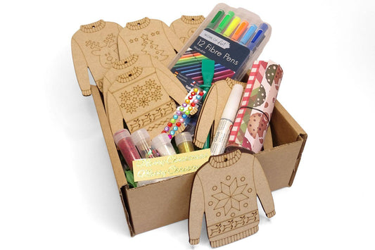 Box full of craft items included in the kit. MDF jumpers etched with Christmas designs and embellishments. On a white background