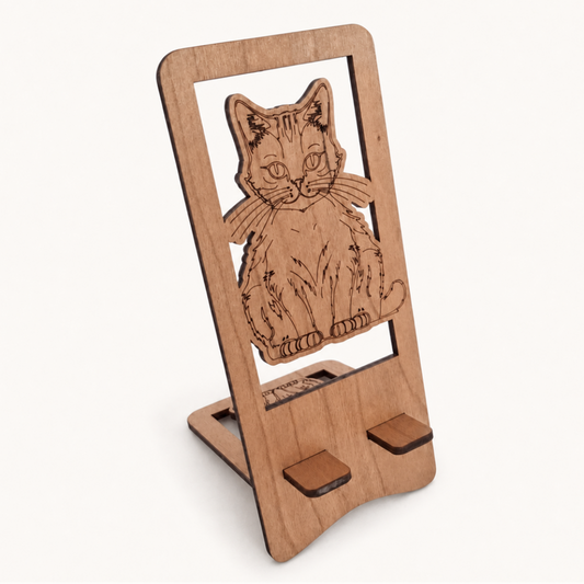 A wooden phone stand with a laser-engraved cat design on the front, shown on a clean off-white background.