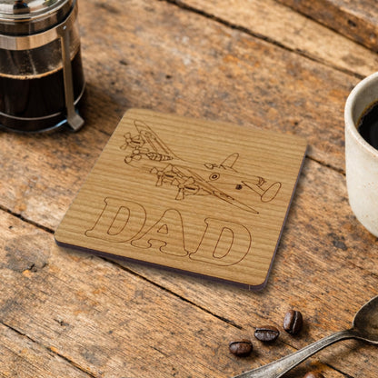 Wooden coaster with airplane design and 'DAD' text on a wooden table with coffee cup, spoon and beans.